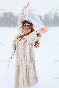 Beautiful Caucasian Russian bride in white dress and in fur coat dancing on snowy field in winter season, Russia